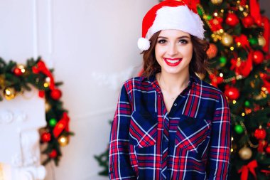 Bir kız şık bir gömlek ve Noel Baba yan tümce şapkası yakınındaki bir Noel ağacı ve bir şömine başında Close-up