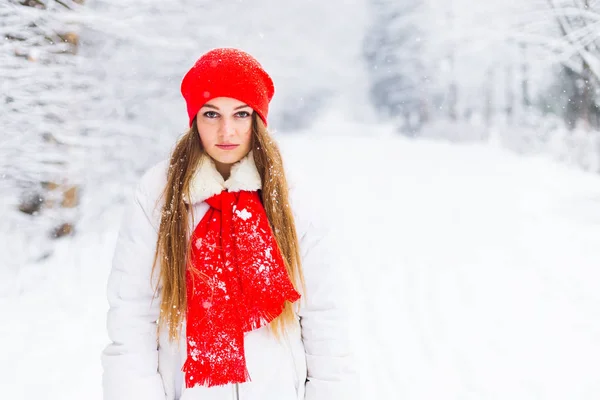 girl in winter clothes with a serious facial expression looks at the camera lens against the background of a snowy park