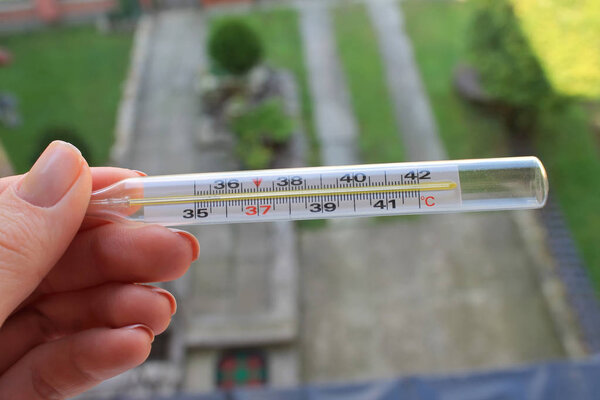 стеклянный ртутный термометр в руках на заднем дворе. измерить термометр ртути.
