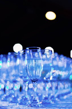 Şeffaf bardakların yakın plan fotoğrafı. Masada birkaç sıra şampanya ve üzerinde mavi ışık parlıyor.