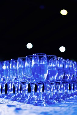 transparent glasses of alcoholic beverages on the table and blue light shines on them clipart