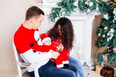 Anne Noel Baba kostümlü bebek şömine ve hediyeler ile ve aralarında bir Noel ağacı, kanepede oturup