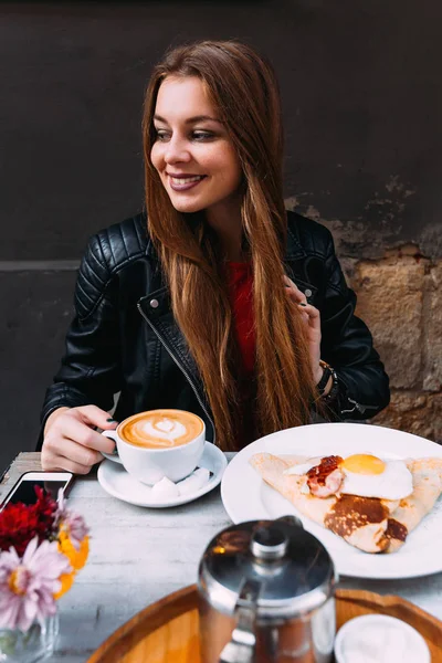 girl with long hair sitting at the cafe\'s table. A delicious breakfast of coffee and egg with bacon on the table