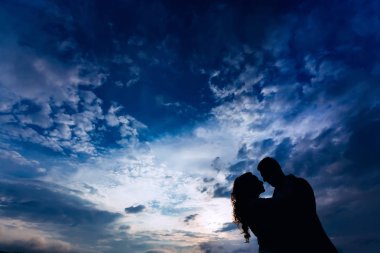 birbirimize arka planı mavi bir gökyüzü bulutlu kucaklayan yeni evliler siluetleri