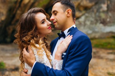 Kayaların arka planında şehvetli bir şekilde kucaklaşan yeni evlilere yakın çekim