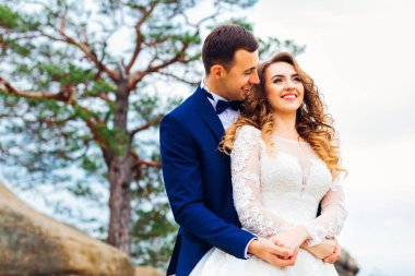 Damadın yakın çekimi, gelini arkadan sarar muhteşem bir manzarayla kayalıklarda.