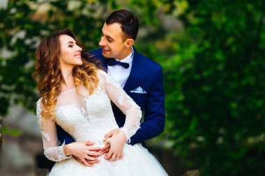 Damat gelini arka taraftan kucaklayan, birbirinize ağaçlar arka plan üzerinde bakın