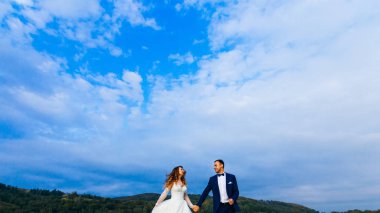 Yeni evliler el ele tutuşup orman ve gökyüzü arka plan karşı göz