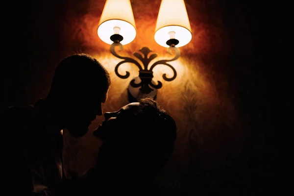 新郎的特写镜头 她把新娘抱在脑后 他们想用黄灯的灯笼在墙的背景上接吻 — 图库照片