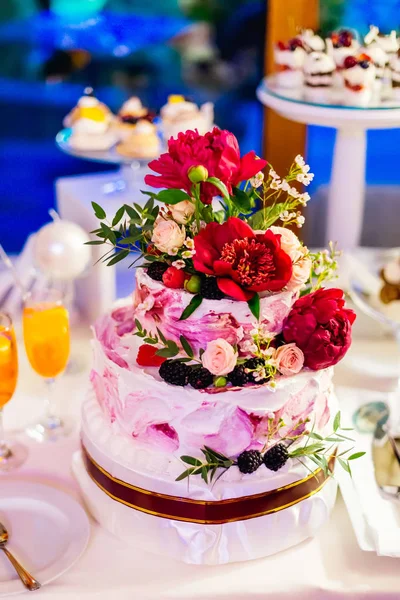A close-up of a tiered cake decorated with red peonies, roses and berries