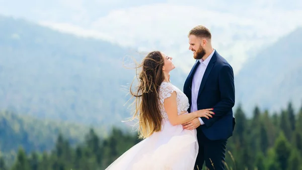 穿着婚纱的新婚夫妇手牵手 在山的背景下互相看着 — 图库照片