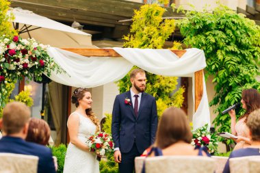 master törenler ve mikrofon konuşuyor yeni evliler görünüyor dekore edilmiş kemer yanında duran. Konuklar ziyaret töreninde bulunması