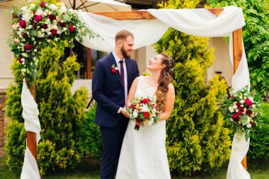 mutlu bir şekilde dekore edilmiş kemer arka planı şirin gülümser ve birbirlerine yeni evliler bakmak