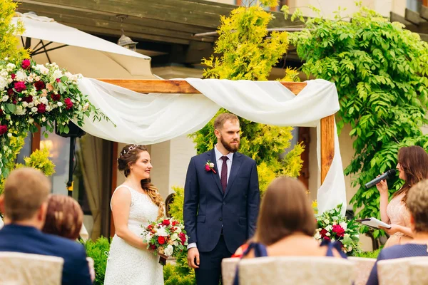 master törenler ve mikrofon konuşuyor yeni evliler görünüyor dekore edilmiş kemer yanında duran. Konuklar ziyaret töreninde bulunması