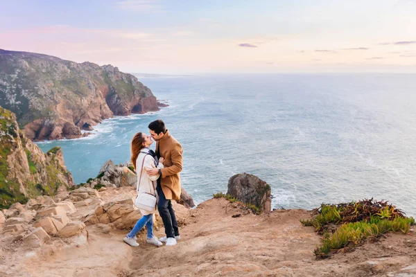 恋爱中的情侣想在石山和傍晚的海洋的背景下亲吻男人和女孩 — 图库照片