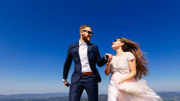 新婚夫妇对着对方微笑 脸上都是太阳镜 他们的特写镜头是这样的 从山上到地平线和万里无云的天空的美丽景色 — 图库照片