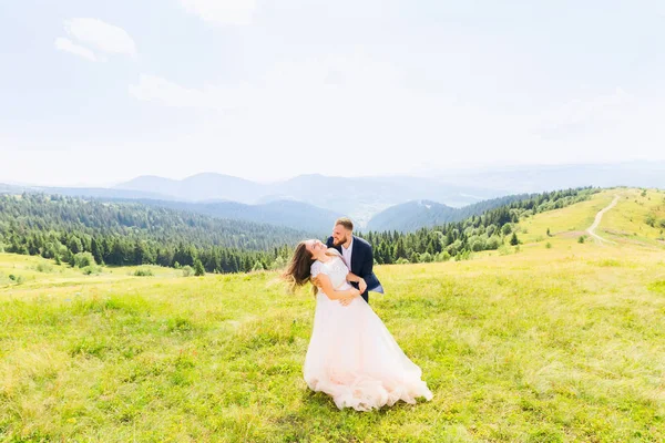 Recém Casados Sorriem Abraçam Entre Prado Topo Montanha Contra Pano — Fotografia de Stock