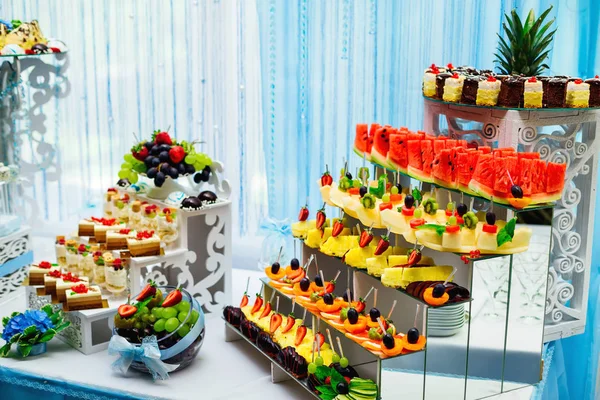 fresh fruits are cut into slices and beautifully decorated with other fruits on the stand. delicious cupcakes on wooden stands