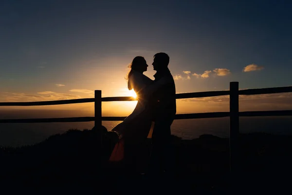 一个男人和一个女人附近的围栏的剪影 在日落和海洋的背景下 他们被抱在栅栏附近 — 图库照片
