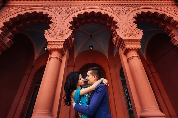 Casal apaixonado perto de um edifício vermelho com arquitetura incrível — Fotografia de Stock