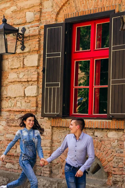 Chica y chico están tomados de la mano y corriendo cerca de un edificio con — Foto de Stock