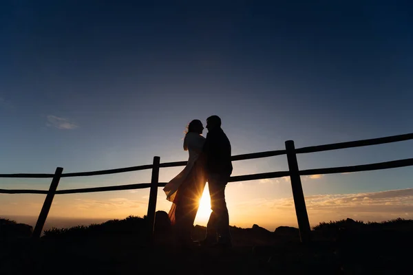 Siluetas de un hombre y una mujer cerca de la valla. Están abrazados. — Foto de Stock