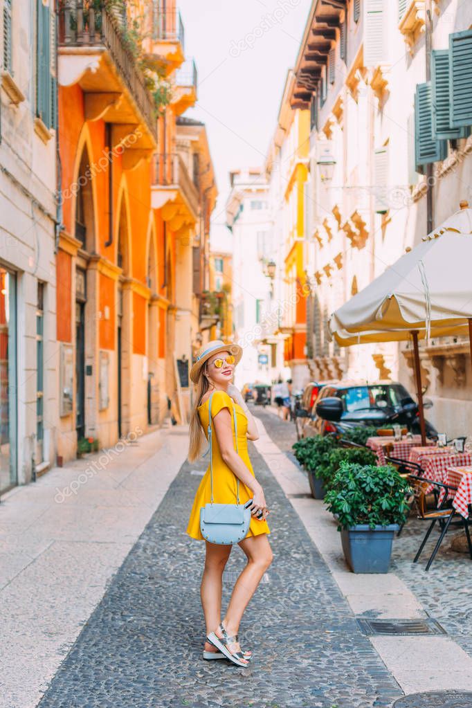 Stylish girl in a yellow dress near a cafe on the street of the 