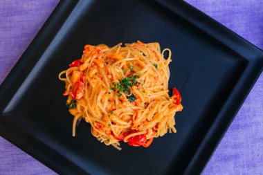 siyah bir kare plaka üzerinde deniz ürünleri ve domates ile makarna. Top vie