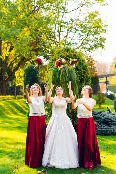 Noiva e damas de honra jogando buquês de casamento no parque — Fotografia de Stock