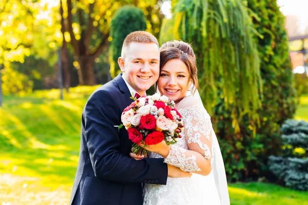 De bruidegom omhelst de bruid, ze lachen en kijken naar de camera. — Stockfoto