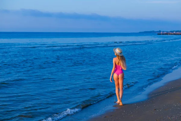Chica en traje de baño rosa caminando en la orilla del mar . — Foto de Stock
