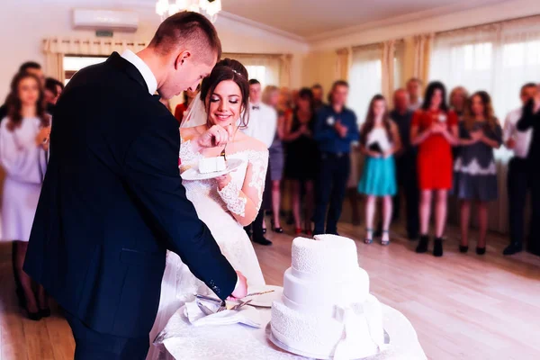 Los recién casados están cortando su pastel de bodas. La novia está comiendo una w —  Fotos de Stock