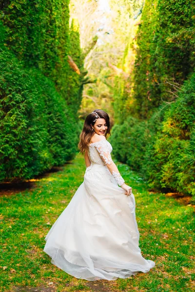 Šťastná nevěsta ve svatebních šatech procházky v parku mezi stromy — Stock fotografie