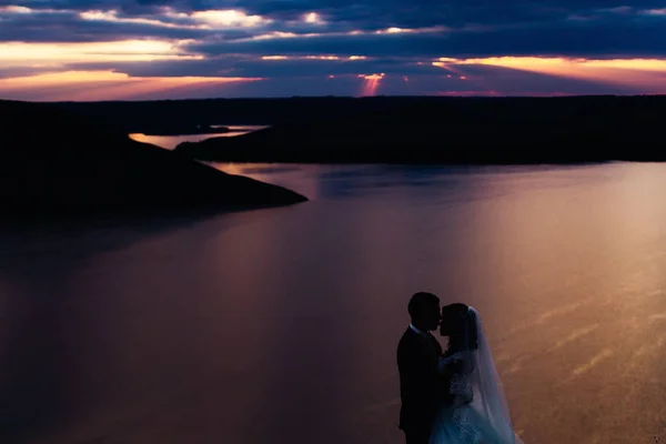 Krásný západ slunce nad řekou. Novomanželé objímalise — Stock fotografie