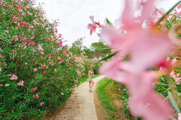 pretty woman walking in dress and boater. park with bushes on wh