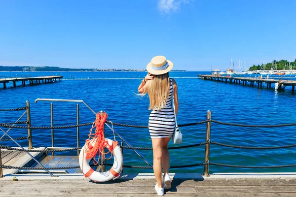 Jeune fille debout sur la jetée près de la bouée de sauvetage et regardant — Photo