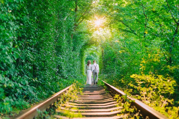 Das verliebte Paar hält sich an den Händen und geht. ein Baumtunnel und eine Schiene — Stockfoto
