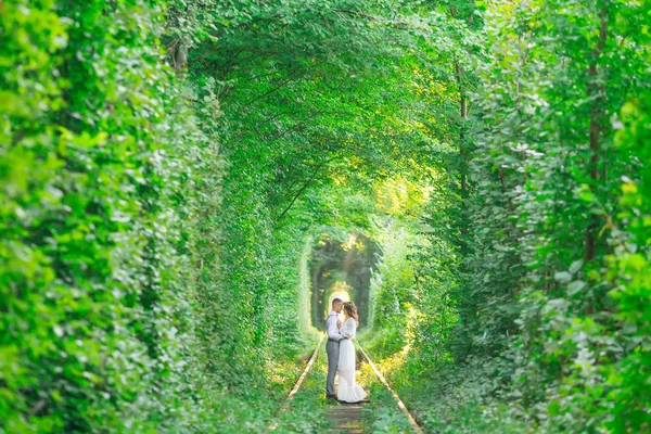 a tree tunnel and a railroad track. the couple in love stand fac