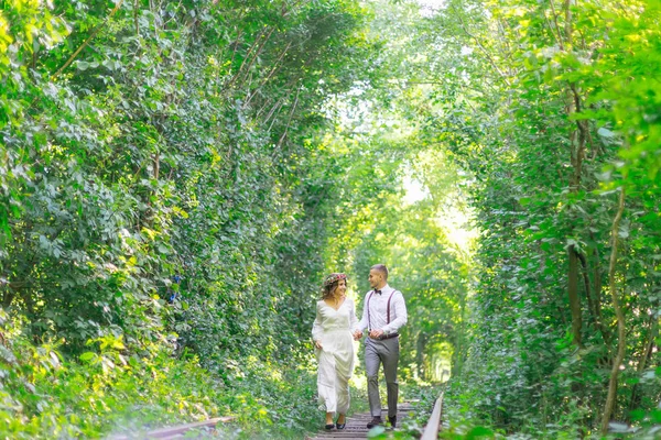 Le couple amoureux se tient la main et court le long du chemin de fer. arbre t — Photo