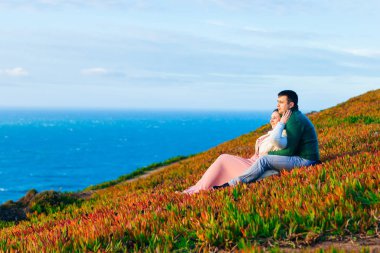 Adam ve kız çimenlerin üzerinde oturuyorlar ve kucaklıyorlar. Adm