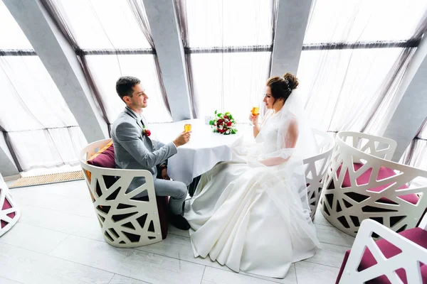 Novomanželé sedí u stolu a pijí šampaňské. Svatební kytice — Stock fotografie