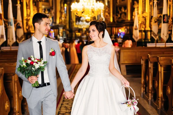 De jonggehuwden houden de handen en verlaat de kerk na de ceremonie — Stockfoto