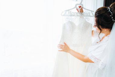 Gelin duvağı takmış güzel gelin gelinliğe dokunuyor.