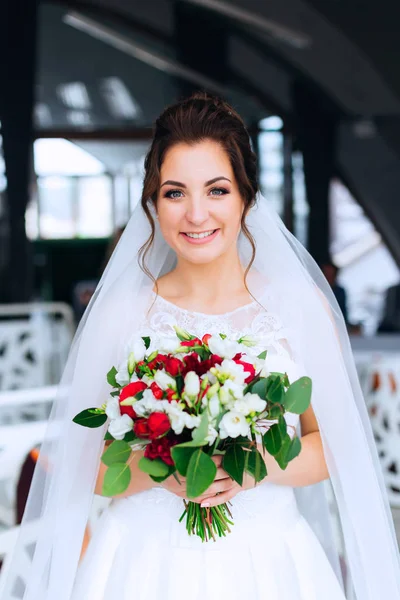 Nevěsta v bílých šatech a svatebních závoji má svatební kytici a — Stock fotografie
