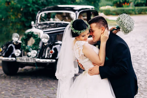 De bruid houdt een bruiloft boeket en de bruidegom knuffels haar op de — Stockfoto