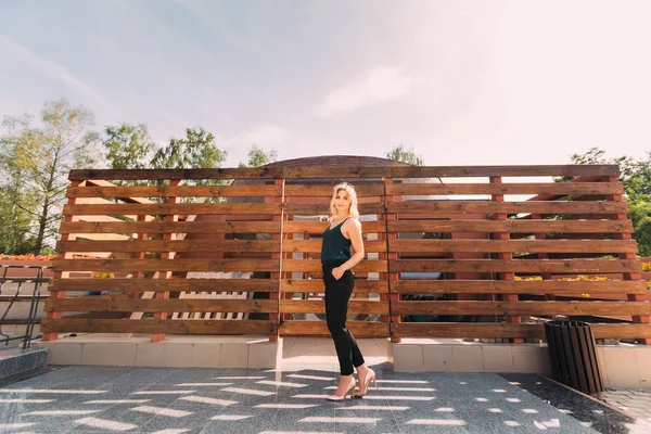 Menina loira elegante posando perto de uma cerca de madeira — Fotografia de Stock