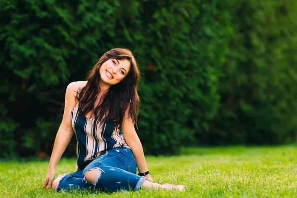 Menina senta-se na grama no parque e sorrir — Fotografia de Stock