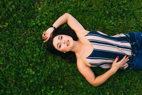 한 청녀가 초록색 잔디 위에 누워 카메라를 바라보고 있었다. 맨 위로 — 스톡 사진