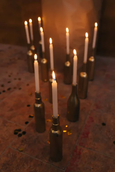 Velas encendidas en botellas de oro en el suelo. confeti —  Fotos de Stock