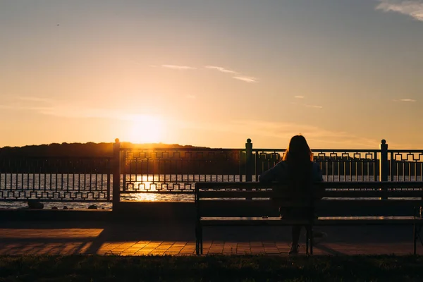 Das Mädchen sitzt auf einer Bank am Ufer eines Sees und bewundert — Stockfoto